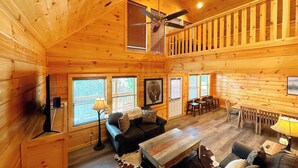 A log cabin interior with a living room, dining area, and a ceiling fan.