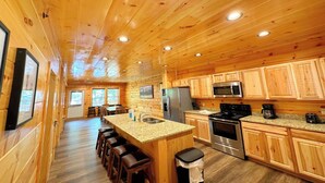 A wooden cabin interior with a kitchen, dining area, and bar stools.