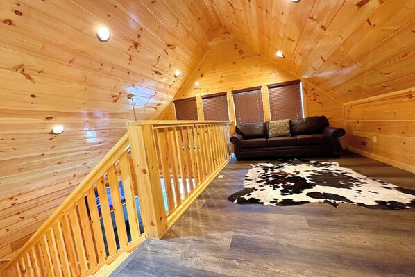 Interior acogedor de una cabaña con una escalera de madera, un sofá de cuero y un tapete de cuero de vaca.