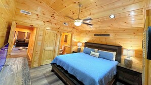A wooden cabin bedroom with a bed, a ceiling fan, and a sign on the wall.