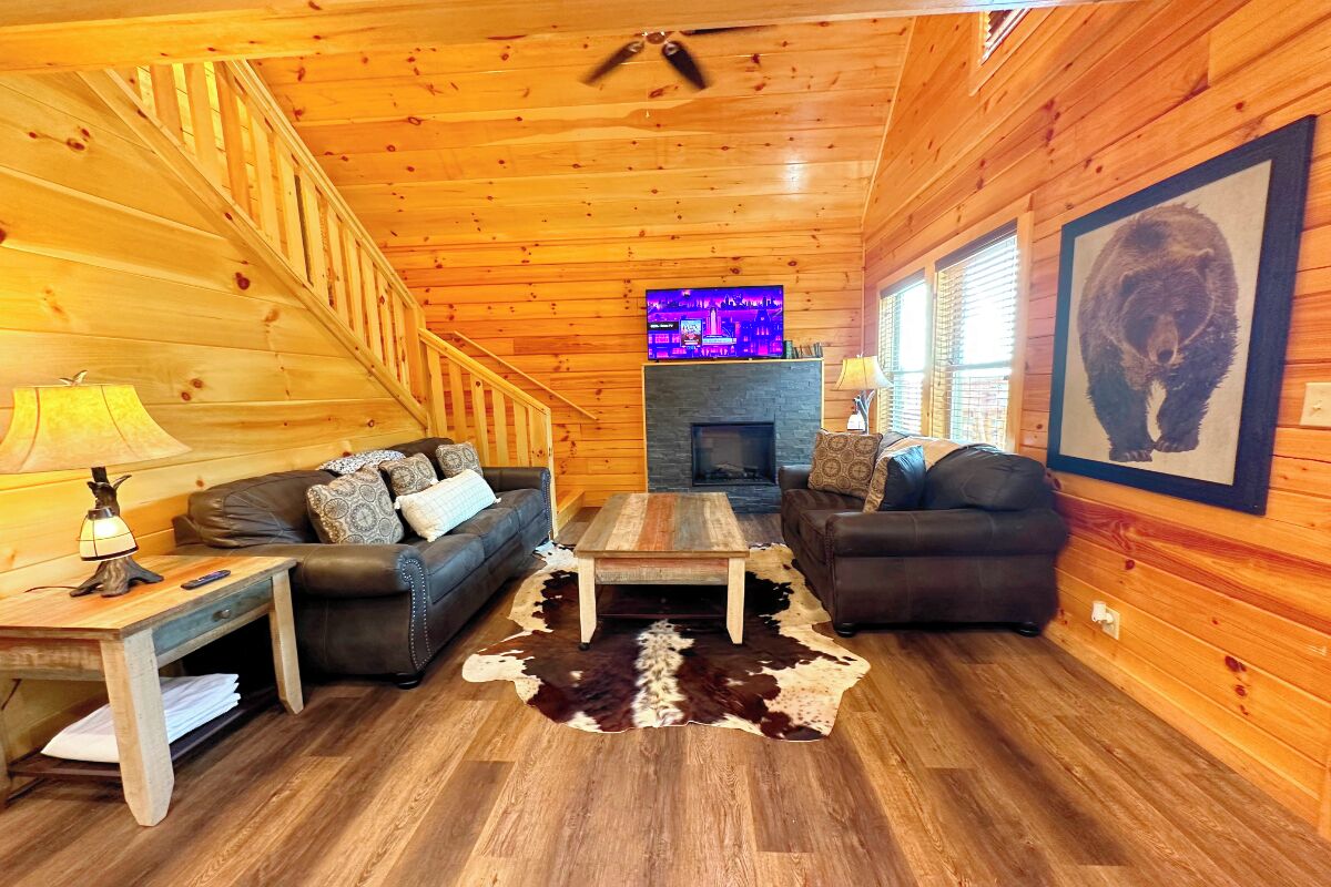 Ein gemütliches Blockhaus-Interieur mit Holzvertäfelung, Kamin, zwei Sofas, einem Couchtisch und einem Fernseher.