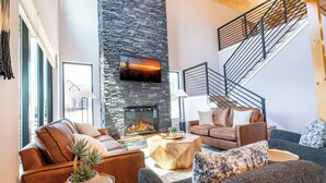 A spacious living room with a stone fireplace, leather sofas, a coffee table, and a staircase. - Gorgeous 4BD Lodge w/ POOL! Hot Tub + Theater (Sevierville)