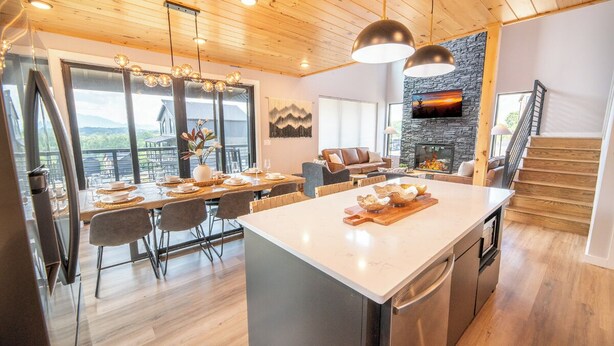 A modern kitchen with a large island, wooden ceiling, and a stone fireplace. - Gorgeous 4BD Lodge w/ POOL! Hot Tub + Theater (Sevierville)