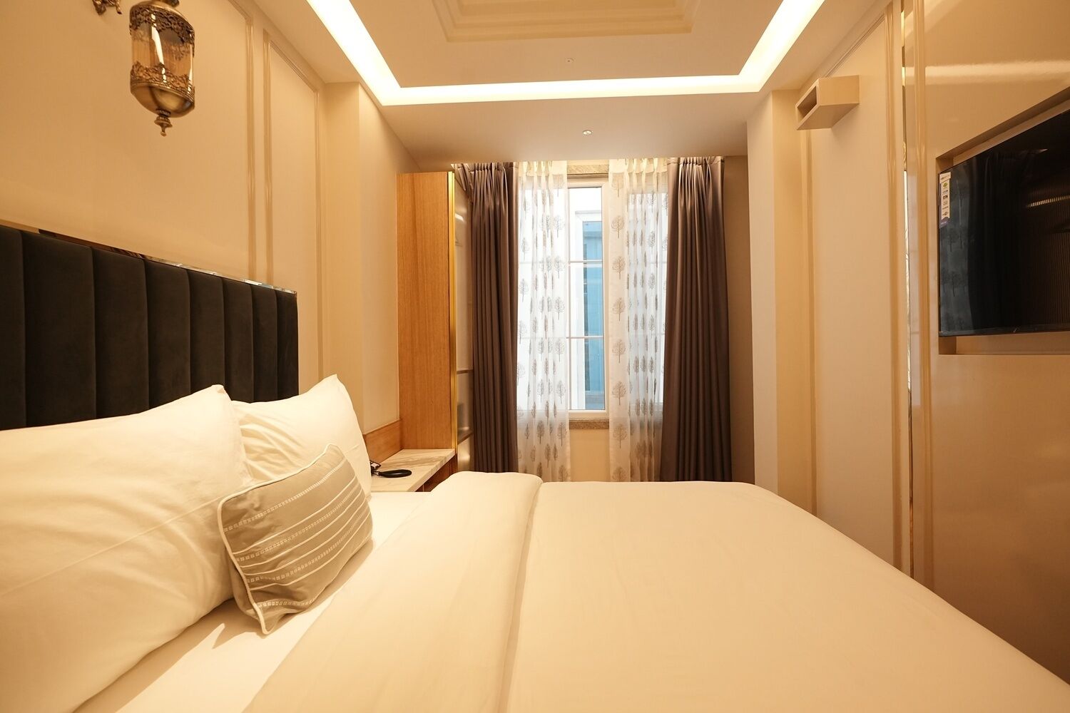 Une chambre d’hôtel avec un grand lit, une table de chevet, une télévision et une fenêtre avec des rideaux.