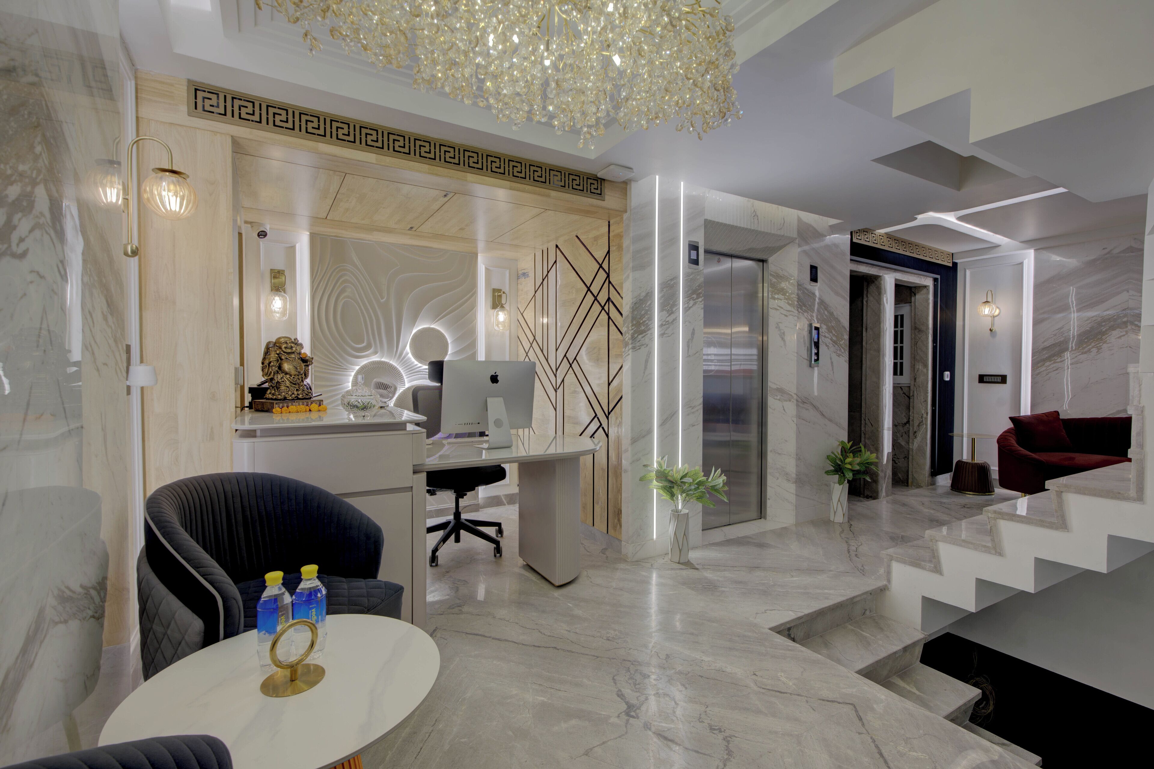 A modern hotel lobby with a marble floor, a desk with a computer, a red sofa, and a staircase.