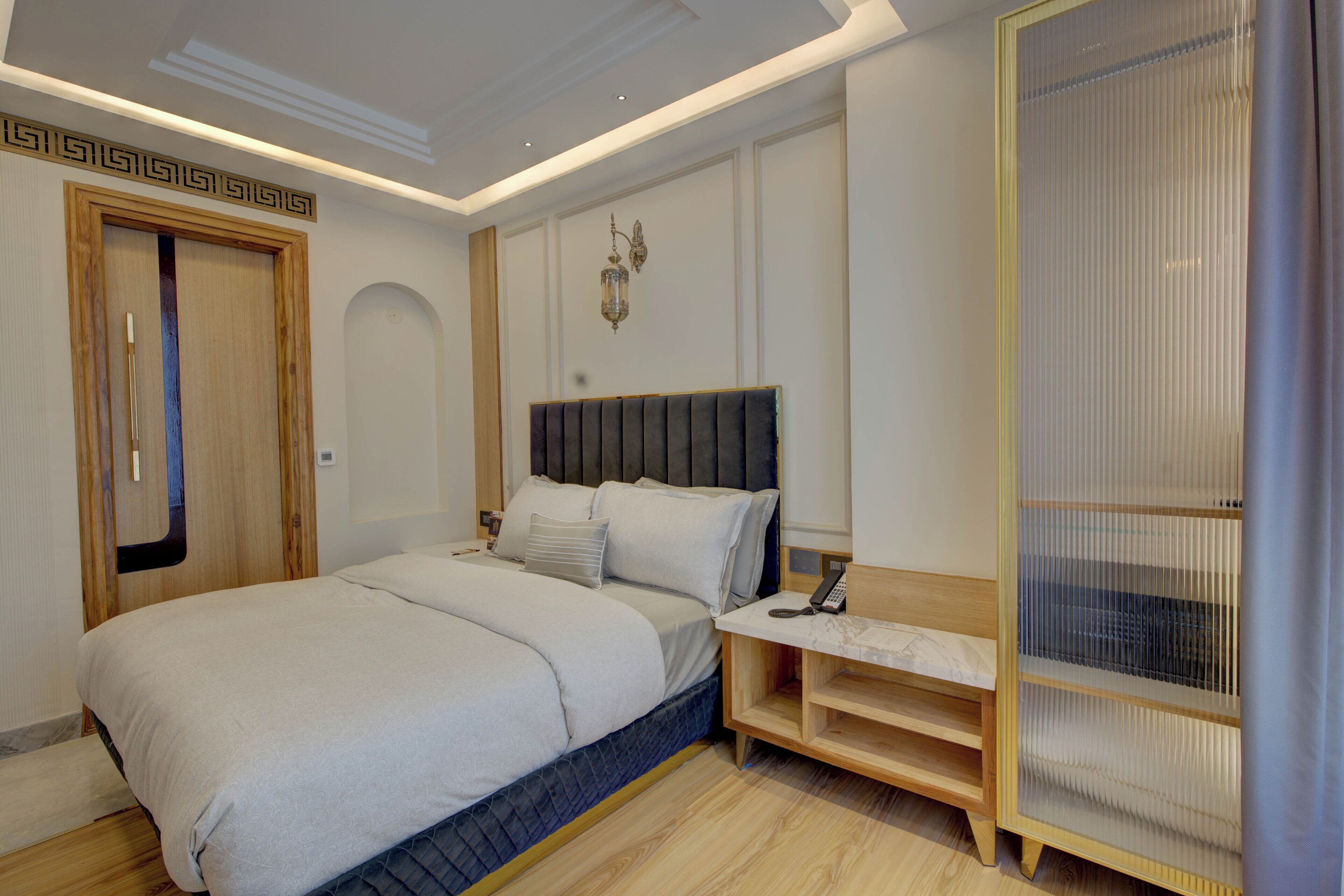 A modern bedroom with a large bed, bedside tables, a wooden wardrobe, and a decorative wall panel.