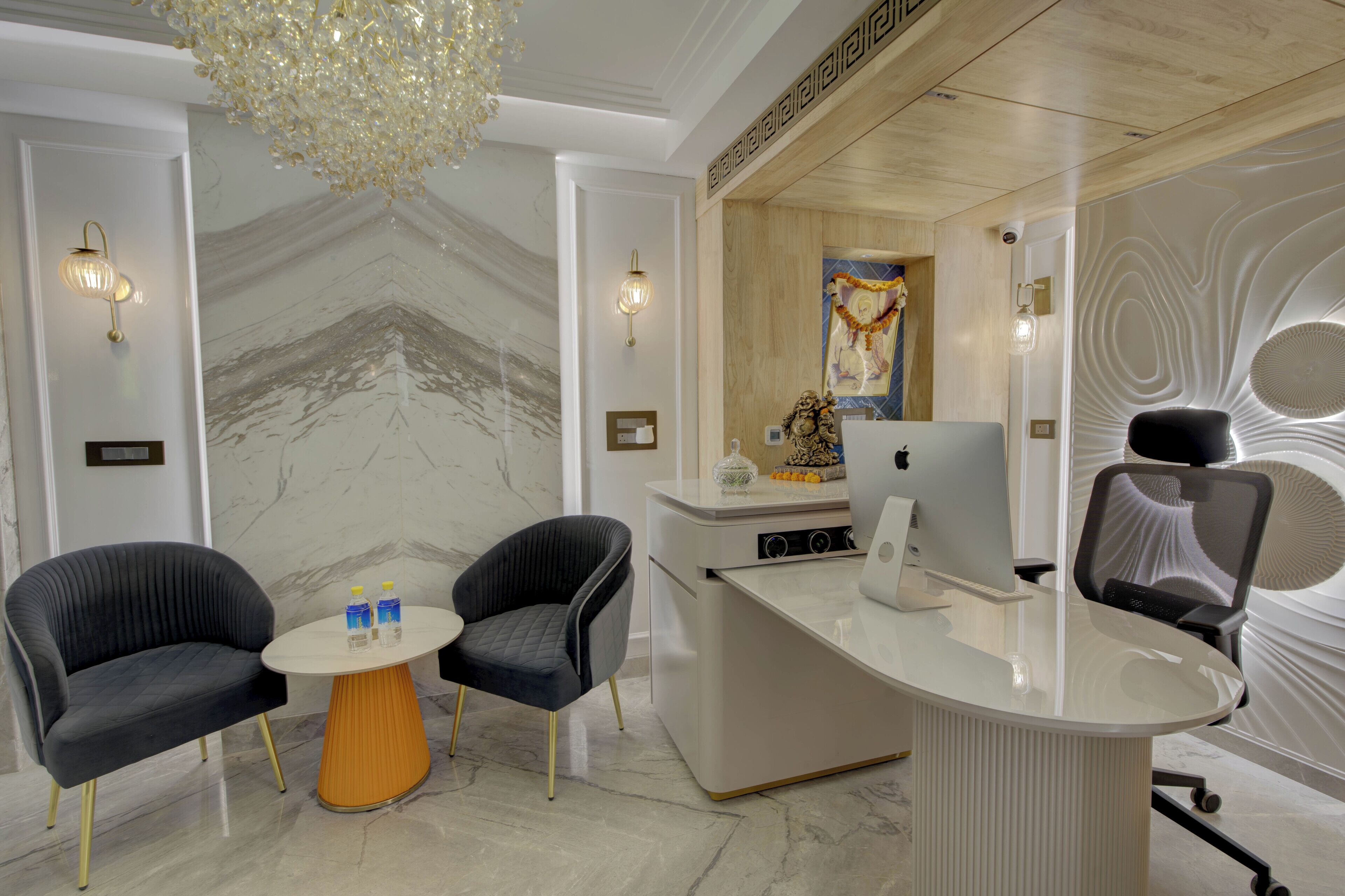 Een modern receptiebalie met twee fauteuils, een marmeren wand en een decoratieve plafondlamp.