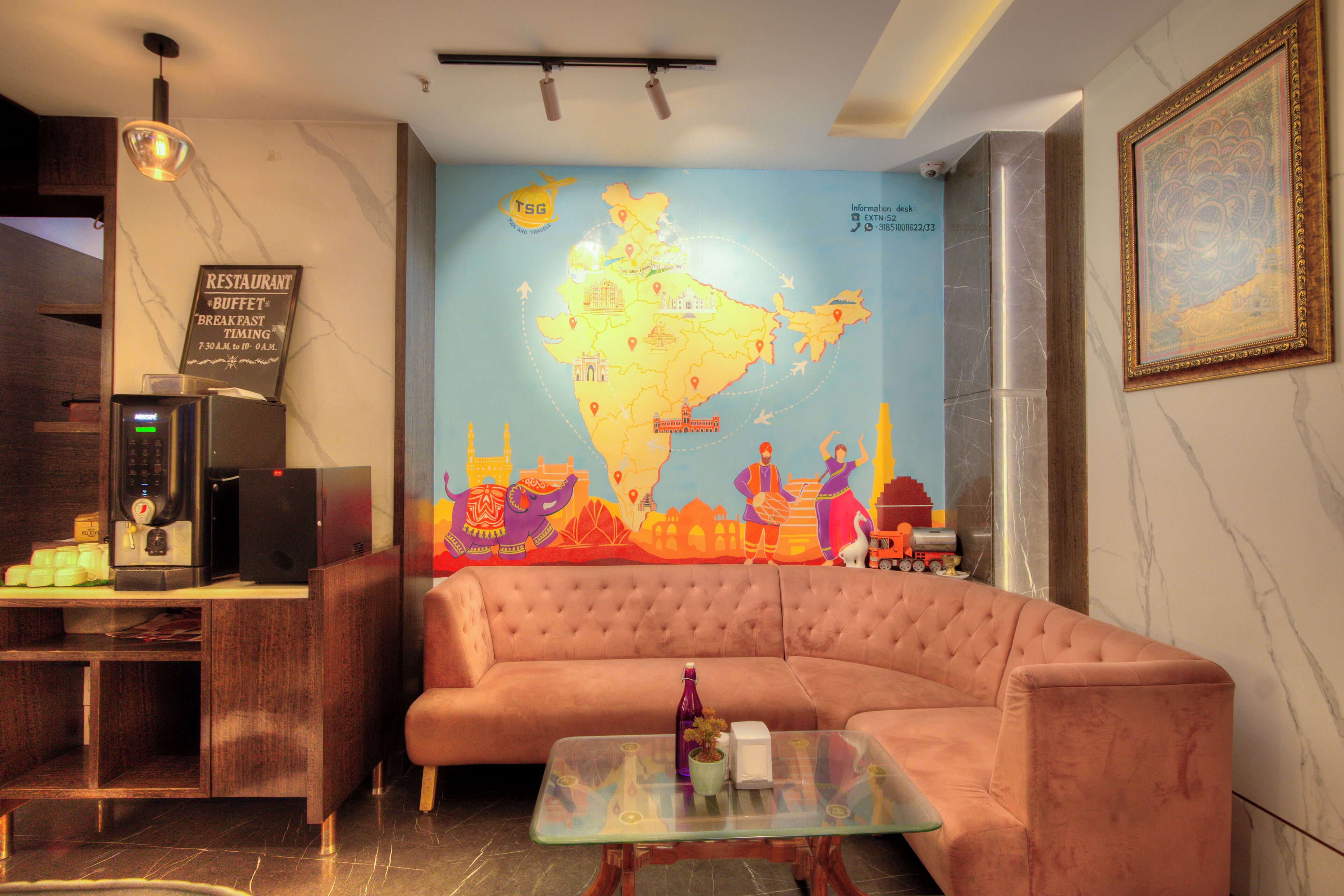 Vestíbulo de hotel con un gran mapa de la India, un sofá, una máquina de café y un cuadro en la pared.