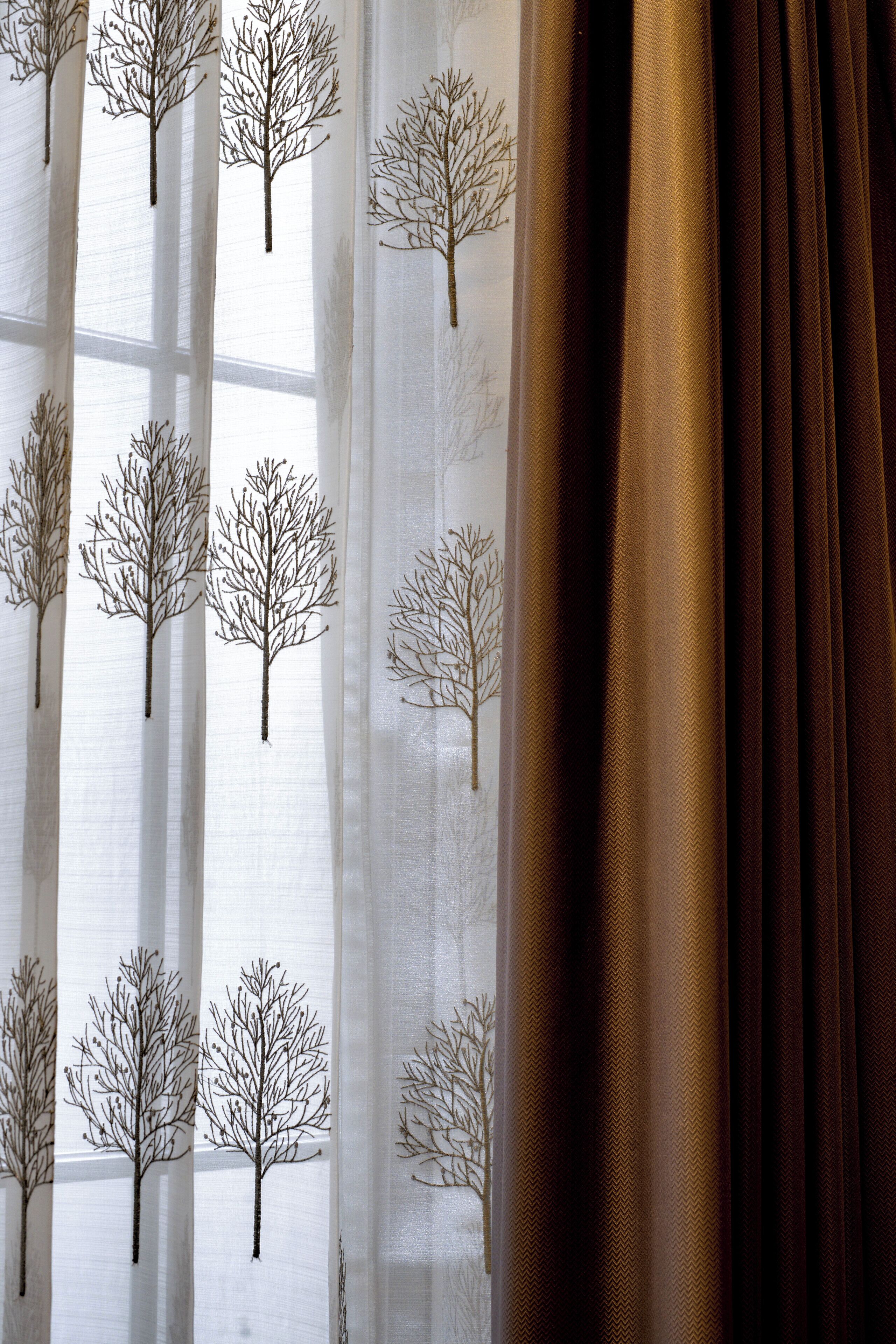 Janela com cortinas finas estampadas com padrão de árvore.