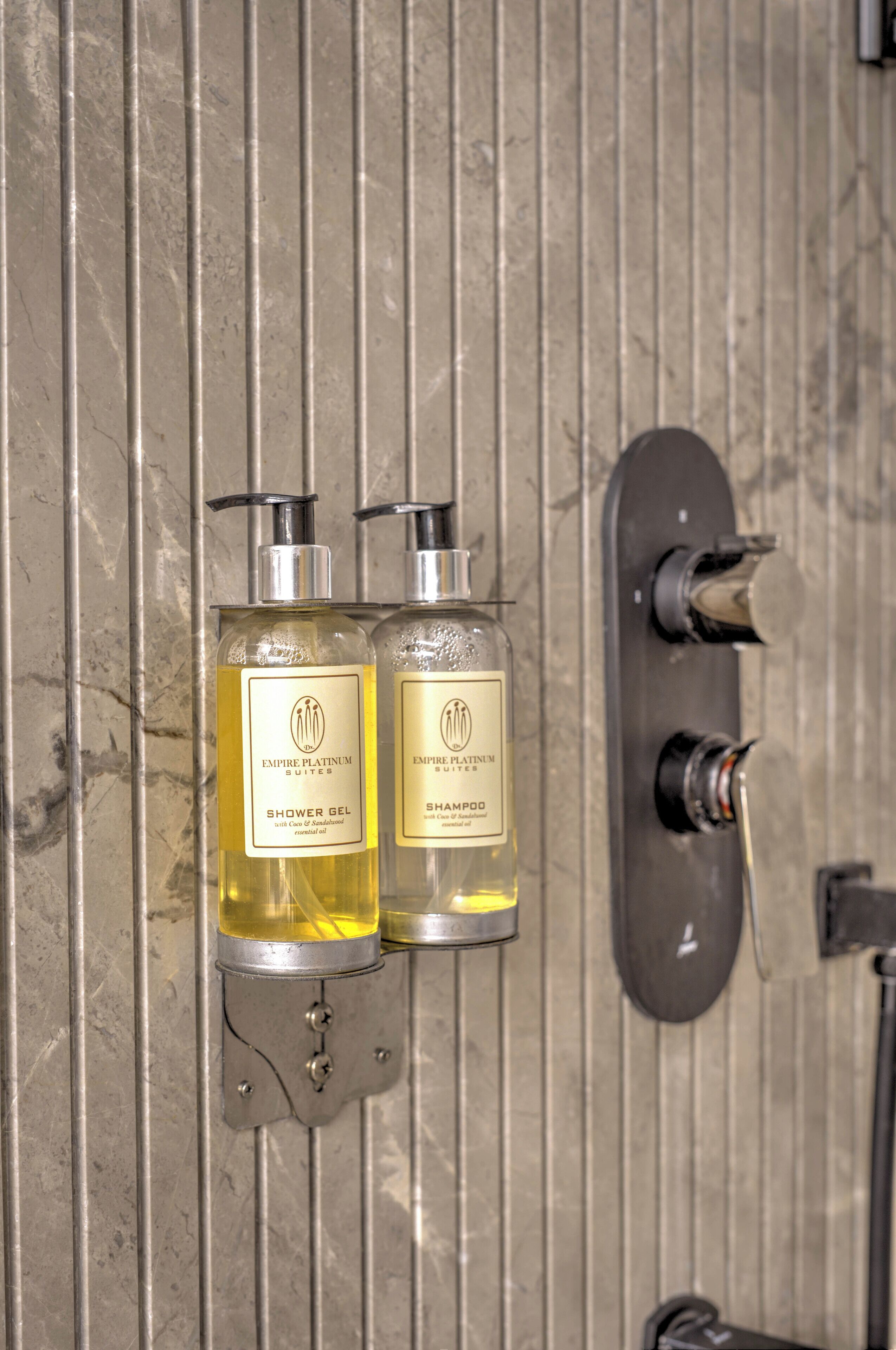 Two bottles of shower gel and shampoo on a metallic wall.