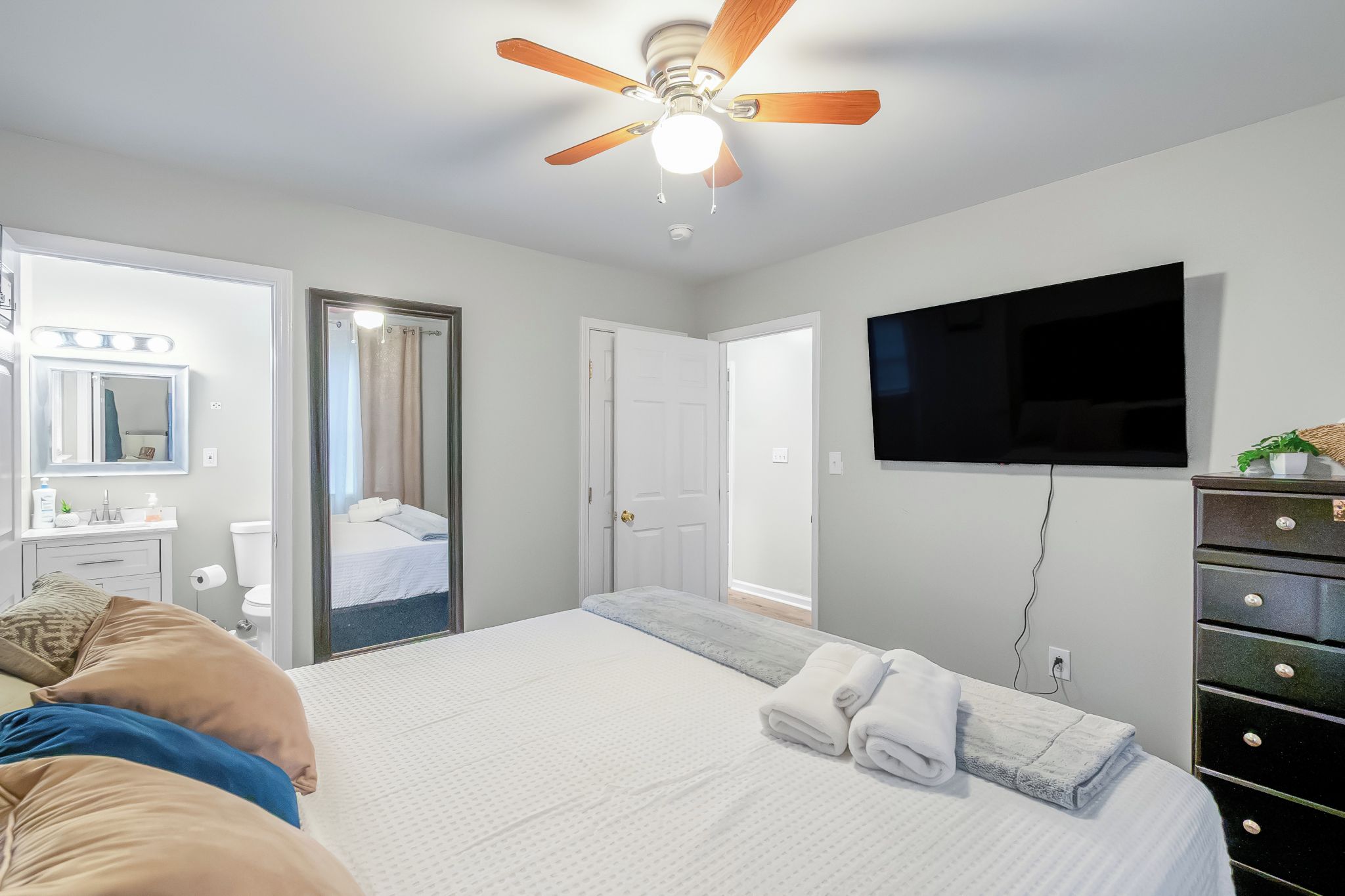 A hotel room with a bed, a television, a ceiling fan, a bathroom with a mirror, and a dresser.