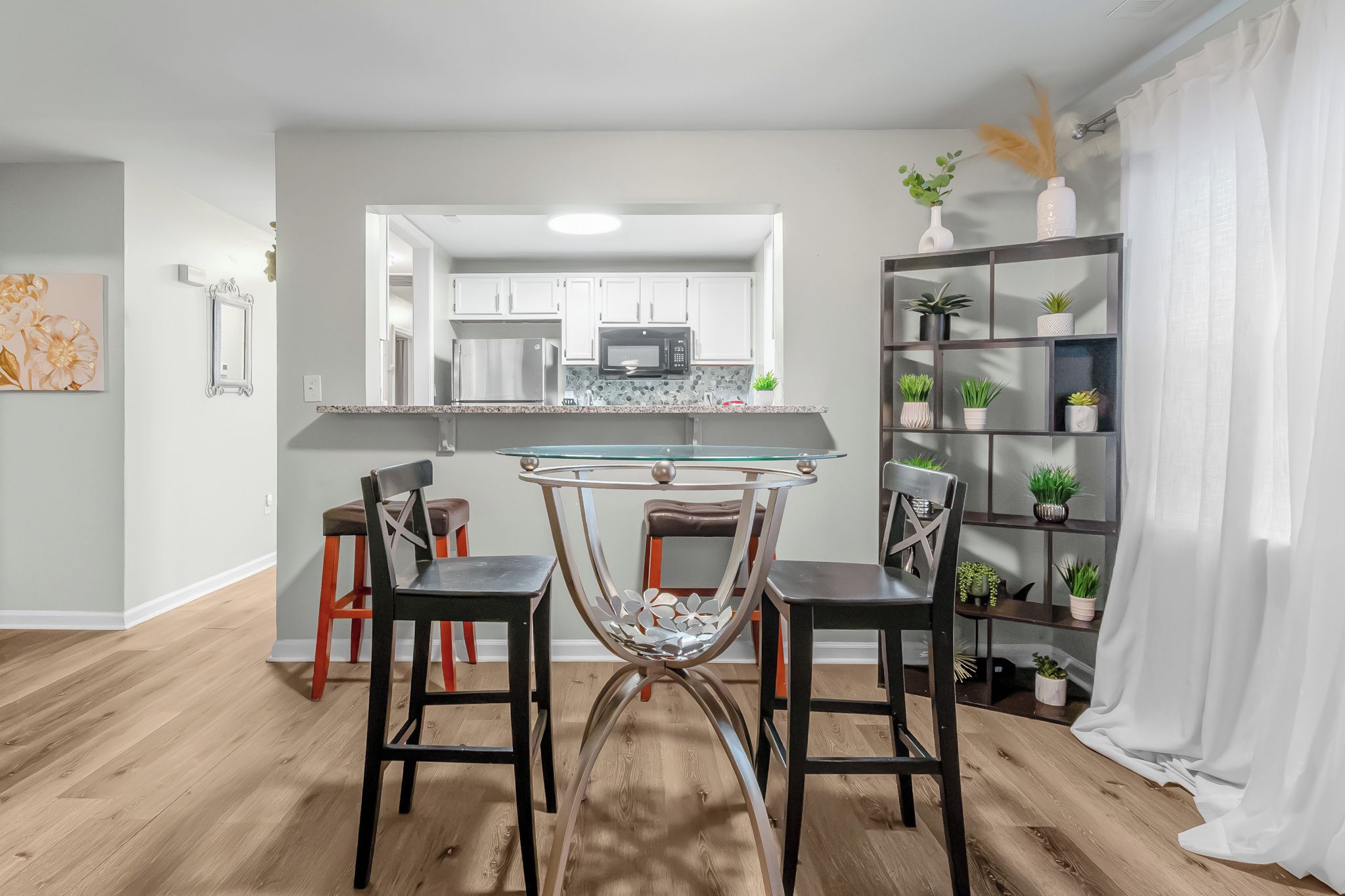 A modern kitchen with white cabinets, a glass-top table, and two bar stools.