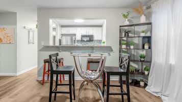 A modern kitchen with white cabinets, a glass-top table, and two bar stools.