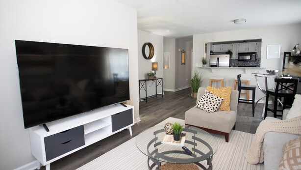 A modern living room with a flat-screen TV, a glass coffee table, and a sofa.