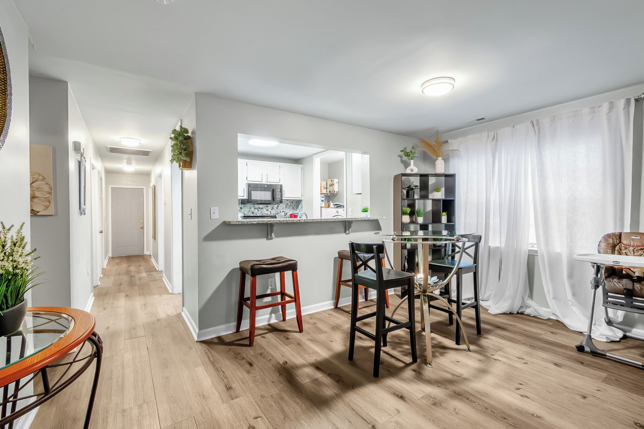 A modern kitchen with a central island, a dining area with chairs, and a living space with a sofa and curtains.