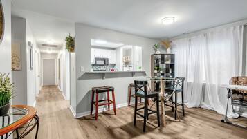 A modern kitchen with a central island, a dining area with chairs, and a living space with a sofa and curtains.