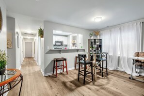 Une cuisine moderne dotée d’un îlot central, d’un coin repas avec des chaises et d’un espace de vie comprenant un canapé et des rideaux.
