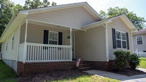 A single-story house with a front porch, brick foundation, and a small front yard.