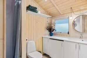 Une salle de bain avec des murs en bois, des toilettes blanches, un lavabo avec un miroir et une fenêtre donnant sur un paysage agréable.