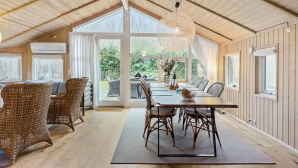 Un comedor con mesa y sillas, ventanas amplias y techo de madera.