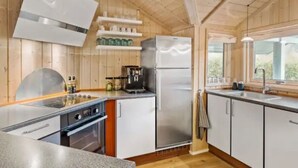 Una cocina moderna con paredes de madera, un refrigerador de acero inoxidable, una cafetera y una ventana que proporciona luz natural.