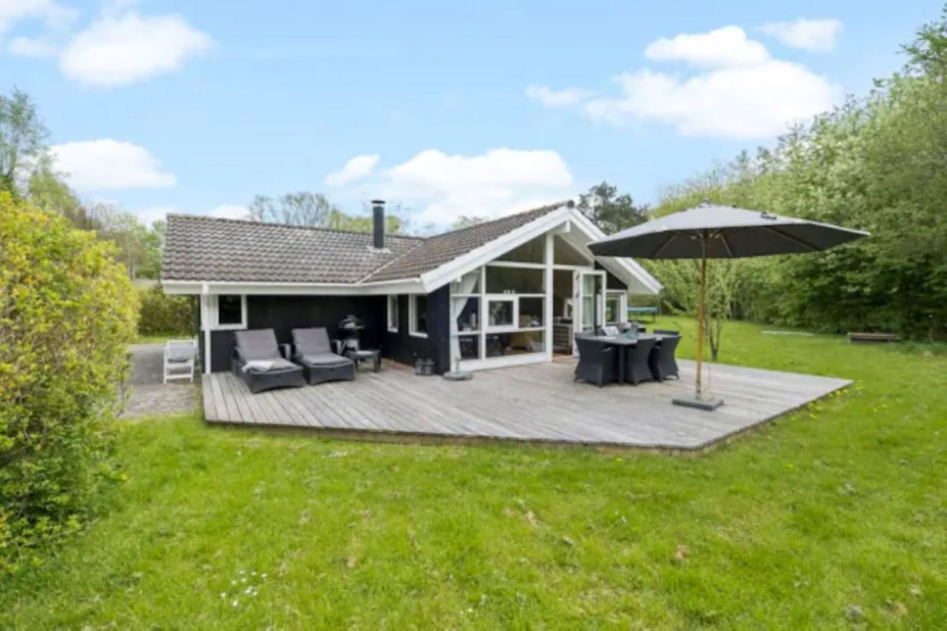 Una casa con terraza, asientos exteriores y un gran paraguas.