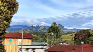 A rural setting with a house featuring a corrugated metal roof, a fenced yard, and a mountainous backdrop. - Hotel Areca (Murillo)