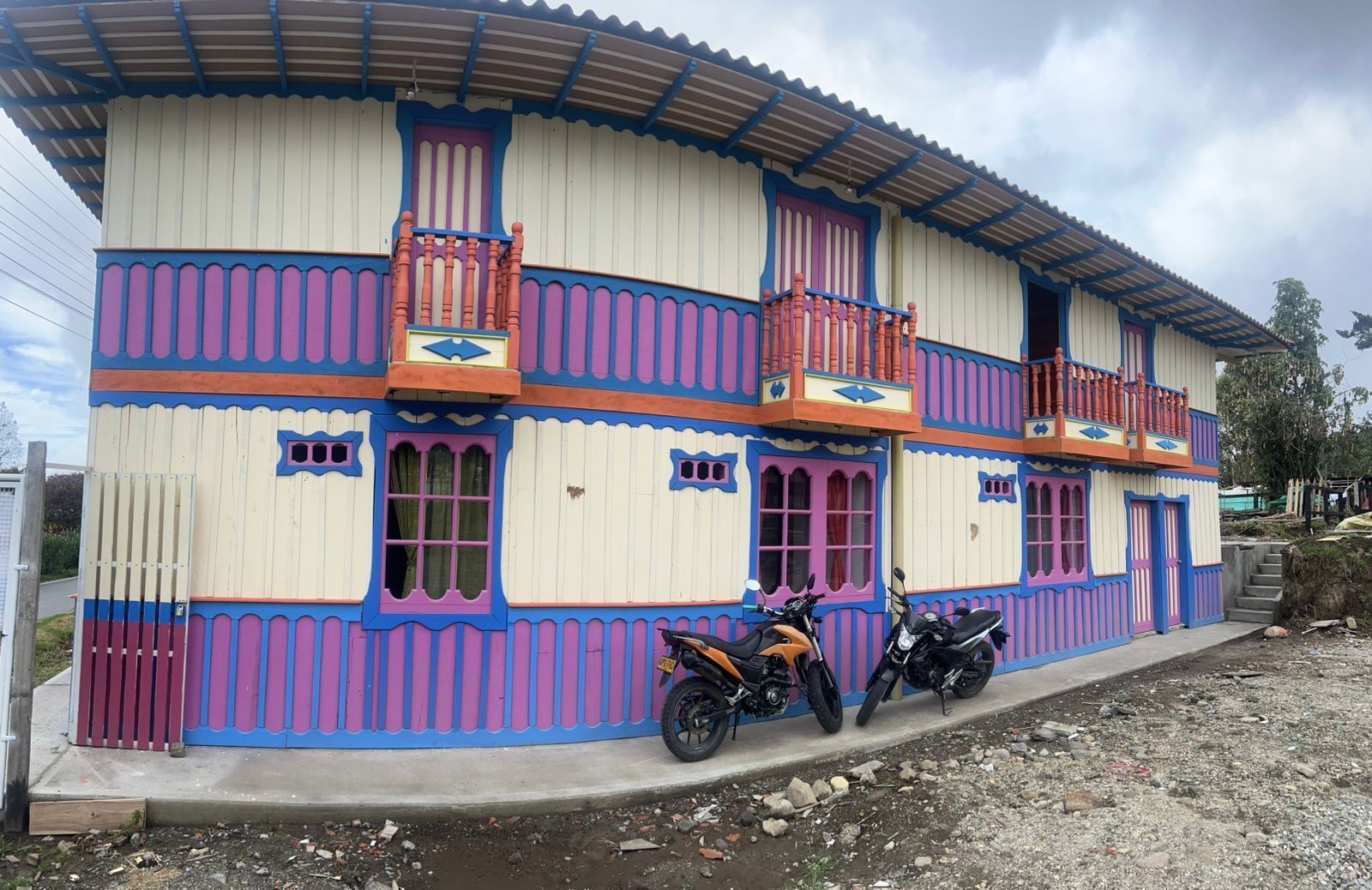 A colorful two-story building with balconies, a gated entrance, and motorcycles parked outside.