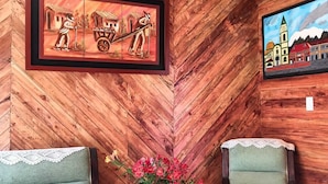 A wooden interior with two armchairs, a small table with a vase of flowers, and two framed artworks on the walls. - Hotel Areca (Murillo)