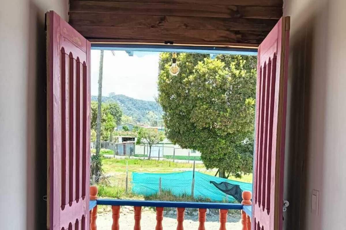 A wooden staircase leading to a balcony with a view of a green landscape and a tree.