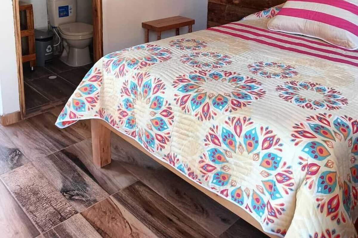 A wooden cabin bedroom with a bed, a small wooden stool, and a wooden shelf.