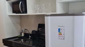 A kitchen with white cabinets, a black countertop, a microwave, a refrigerator, and a sink. - Villas do Porto - 109 by La Playa (Ipojuca)