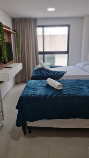 A hotel room with two beds, a desk, and a window with curtains.