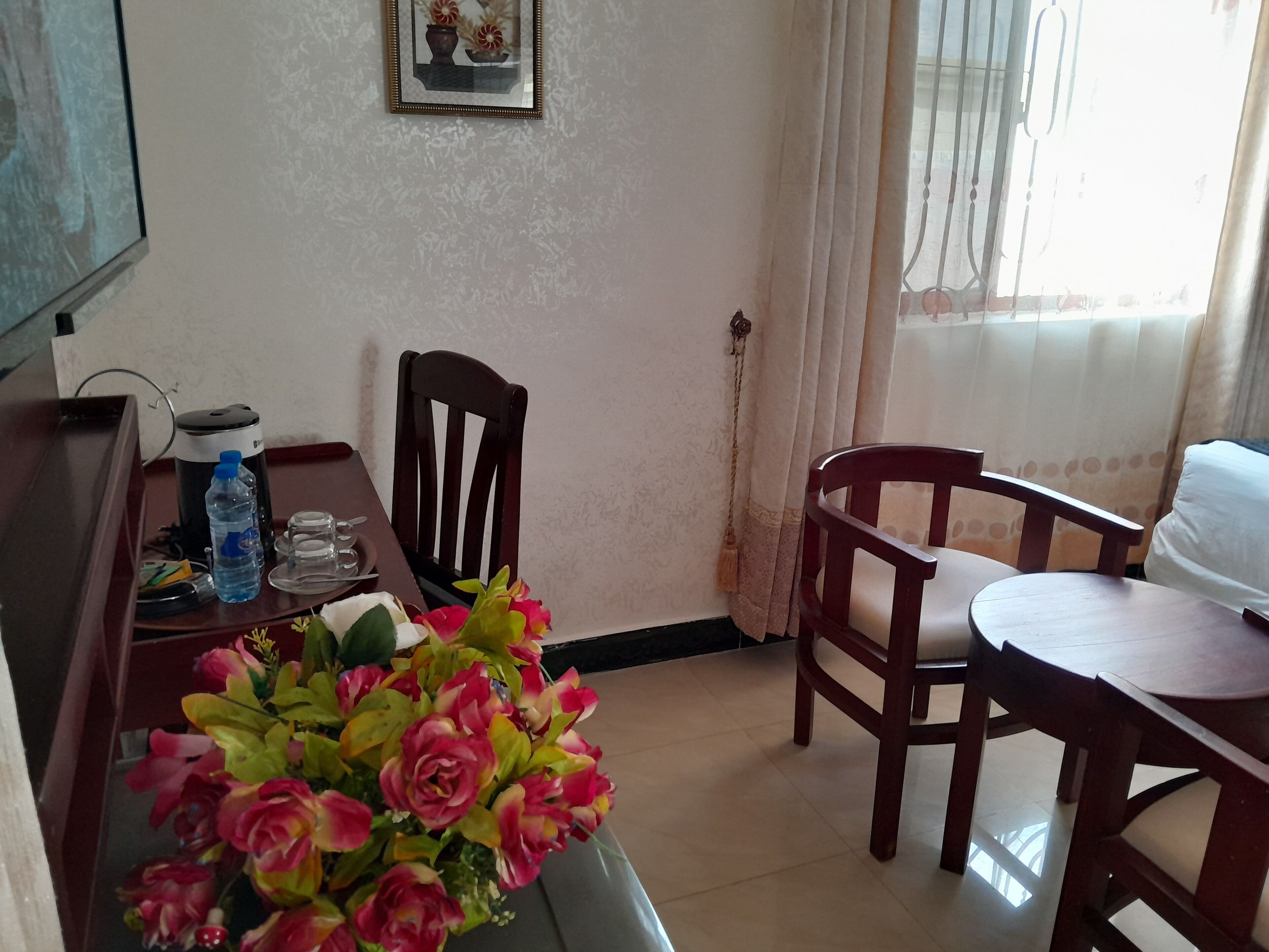 Habitación de hotel con una mesa de comedor, sillas, una botella de agua, un florero, una cafetera y un cuadro en la pared.