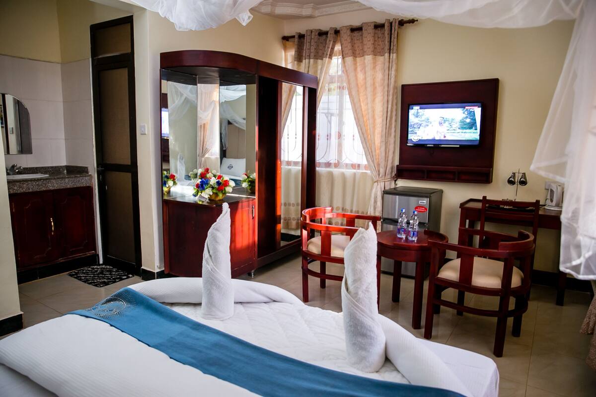 A hotel room with a bed, a desk with a chair, a television, and a bathroom with a mirror and sink.