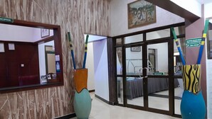 A reception area with a reception desk, a mirror, and a painting on the wall. There are two large vases with colorful patterns in the foreground. - KIBO PEAK PALACE HOTEL (Morogoro)