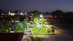 A nighttime view of a landscaped garden with a fountain, palm trees, and various sculptures. - KIBO PEAK PALACE HOTEL (Morogoro)