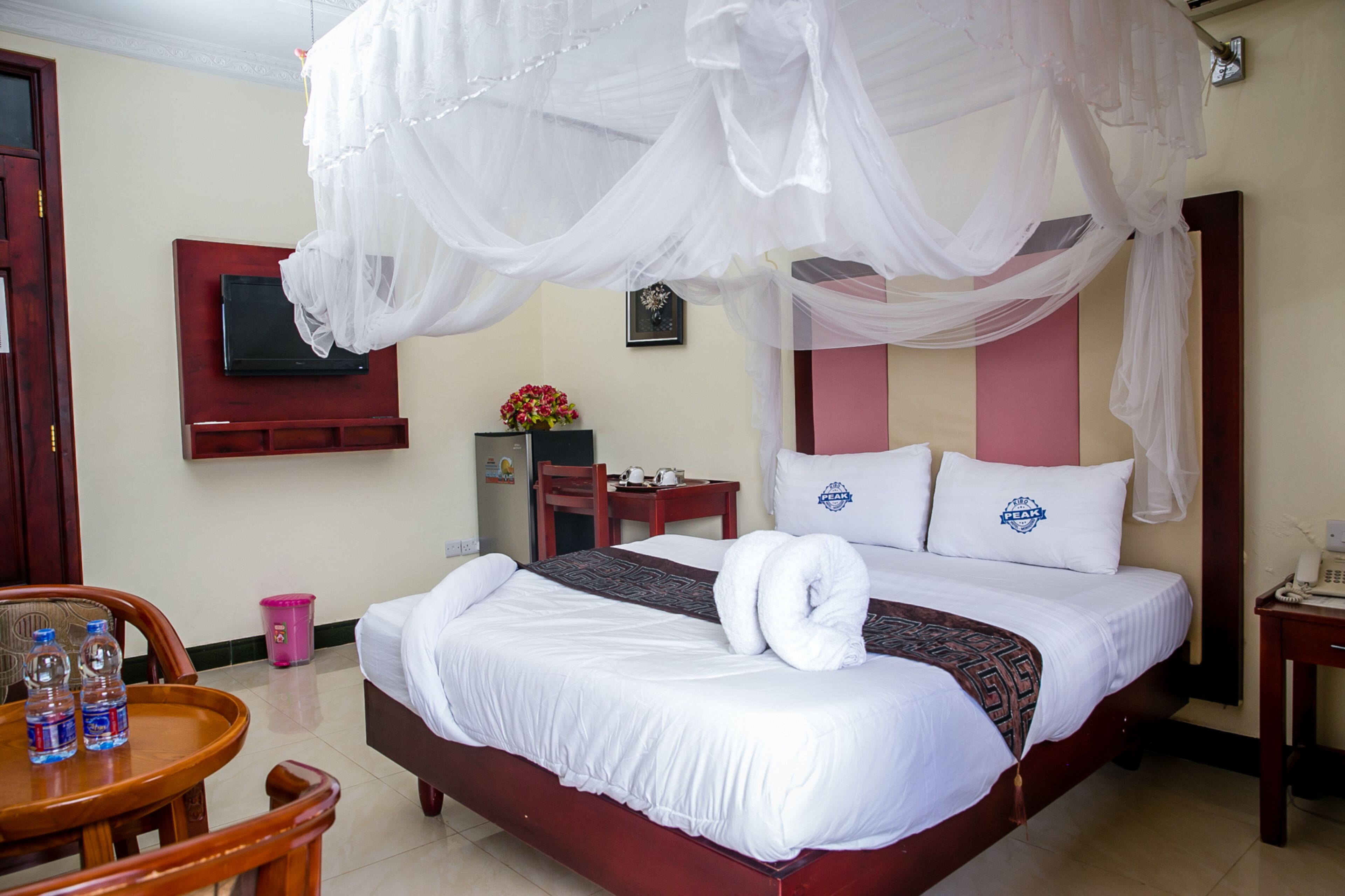 Habitación de hotel con cama, televisor montado en la pared, una mesita con botellas de agua y una silla.