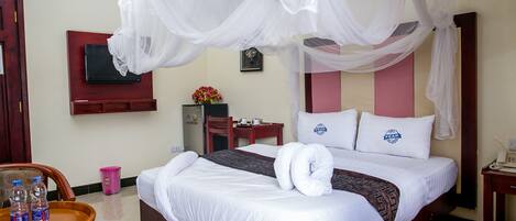 Habitación de hotel con cama, televisor montado en la pared, una mesita con botellas de agua y una silla.