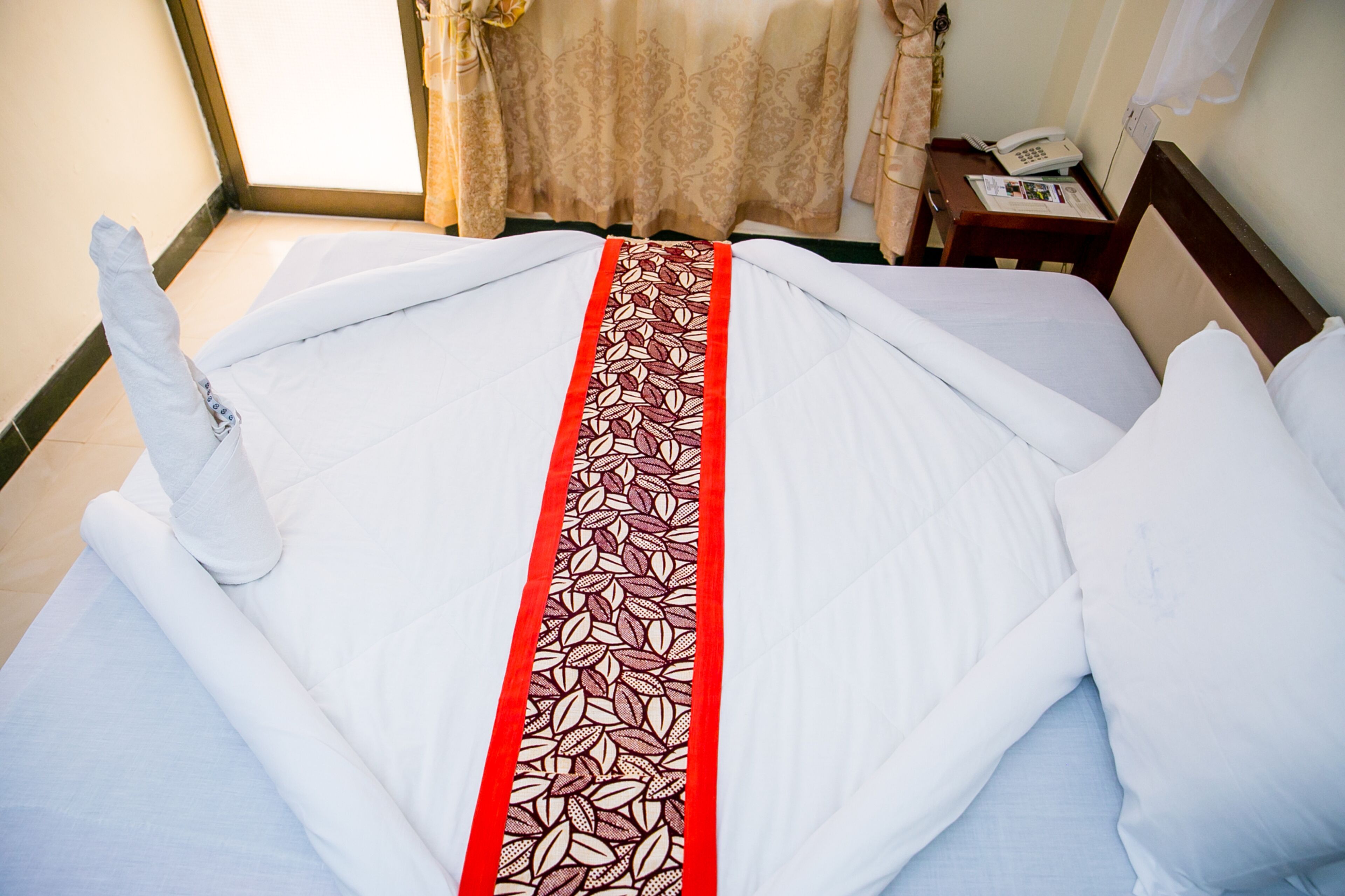 Un lit bien fait, avec un couvre-lit aux motifs de feuilles rouges et blanches, un oreiller blanc et une tête de lit en bois.