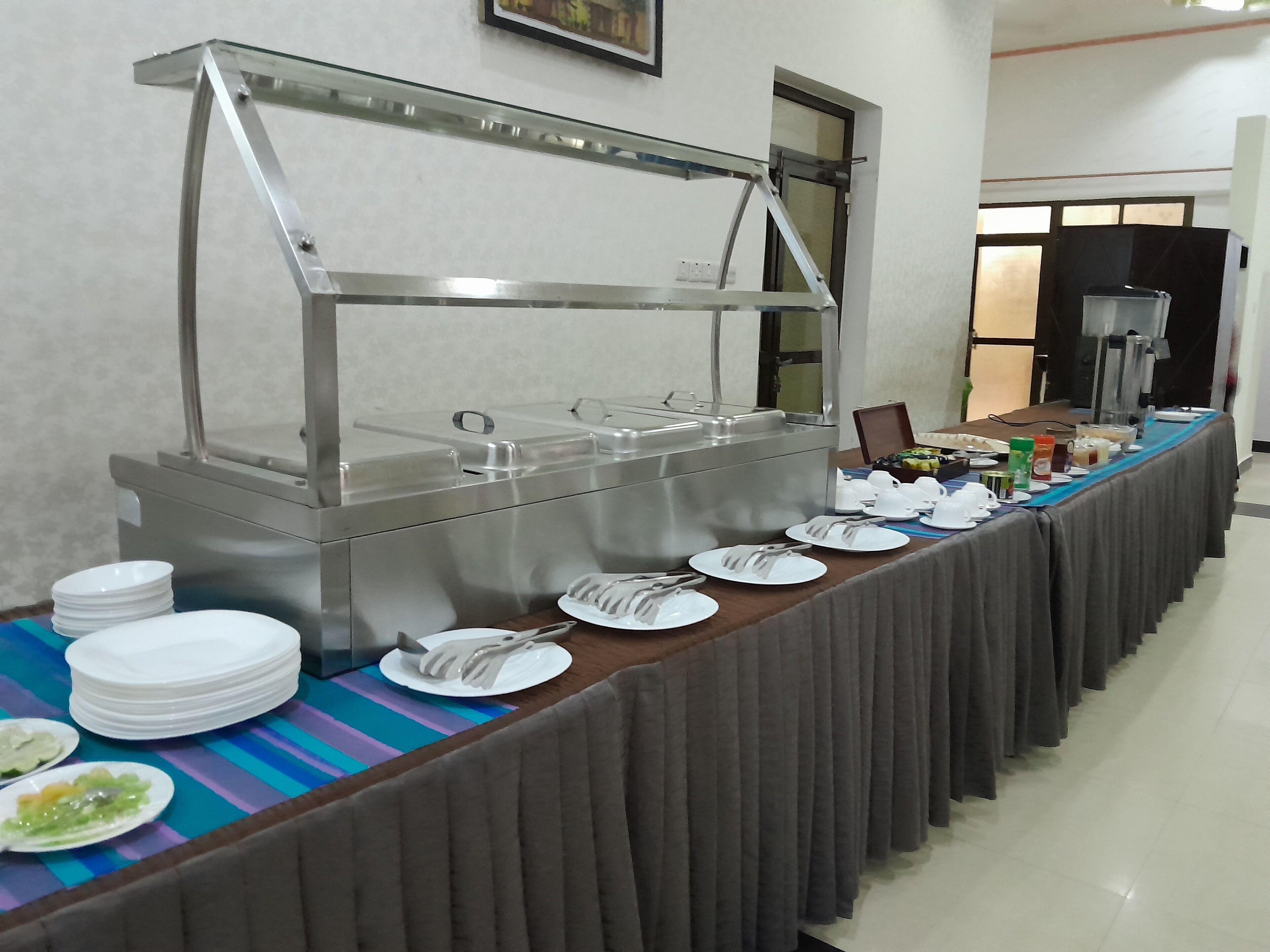 A buffet setup with a stainless steel counter, plates, utensils, and a variety of food items.