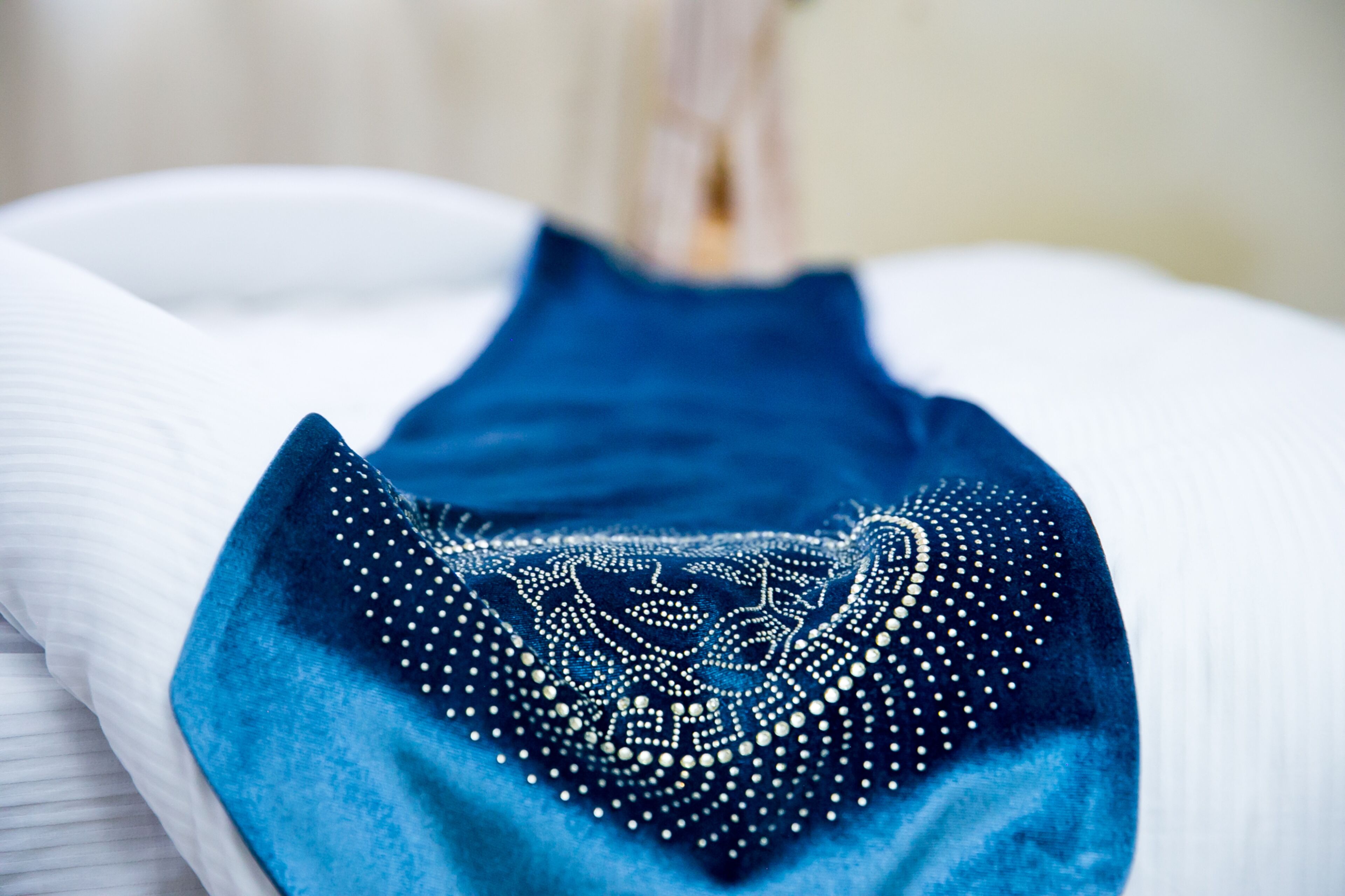 Un lit bien fait, recouvert d’une couverture bleue ornée d’un motif décoratif.