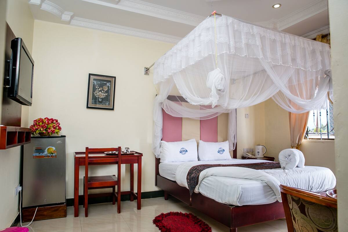 A bedroom with a bed, a bedside table, a chair, a TV, and a refrigerator.
