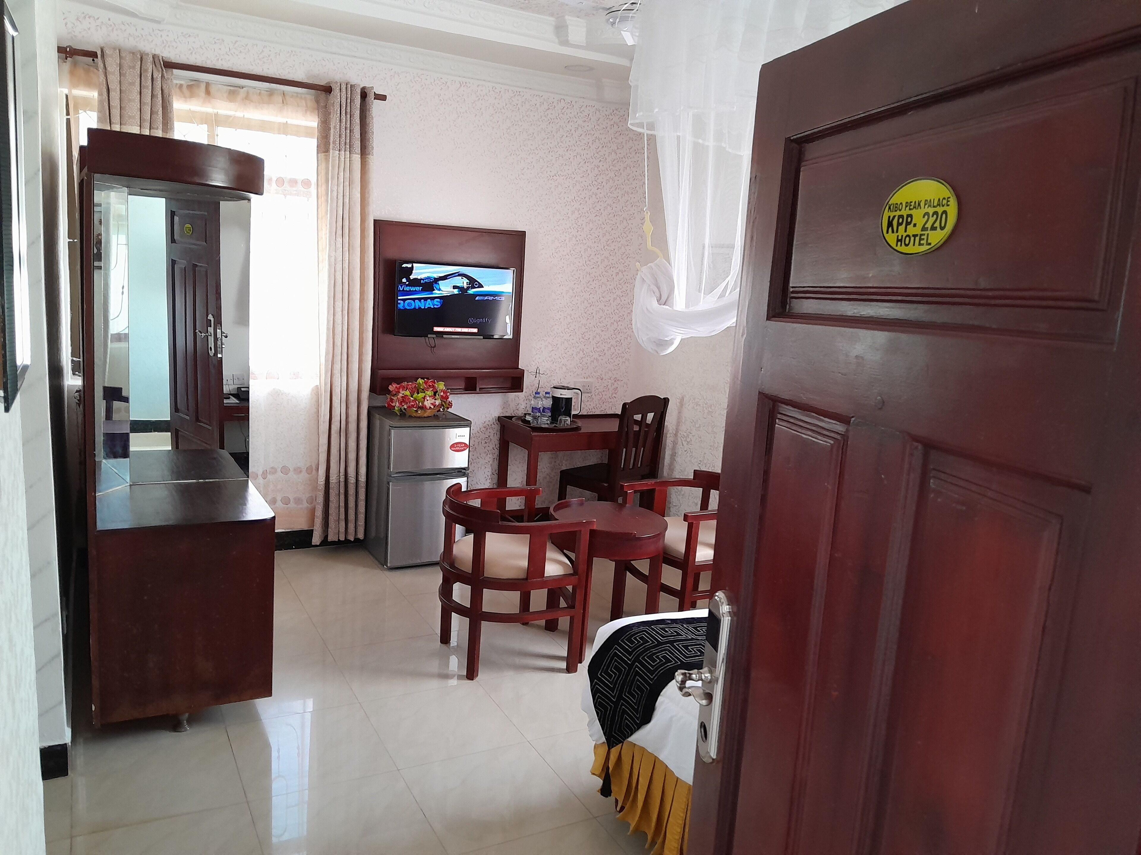 A hotel room with a dining area, a television, a minibar, and a bed with a blanket.