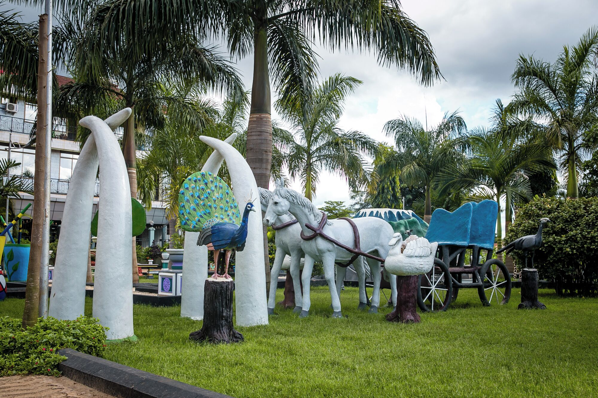 Un jardín de esculturas con pavos reales, caballos y un carruaje.