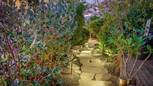 Un chemin de pierre bordé d’une végétation luxuriante mène à une terrasse en bois.
