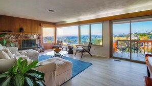 Un vaste salon doté d’une cheminée en pierre, de grandes fenêtres offrant une vue sur la ville et d’un balcon aménagé avec du mobilier d’extérieur.
