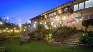 Une maison à deux étages avec un balcon, un jardin bien entretenu et des guirlandes lumineuses.