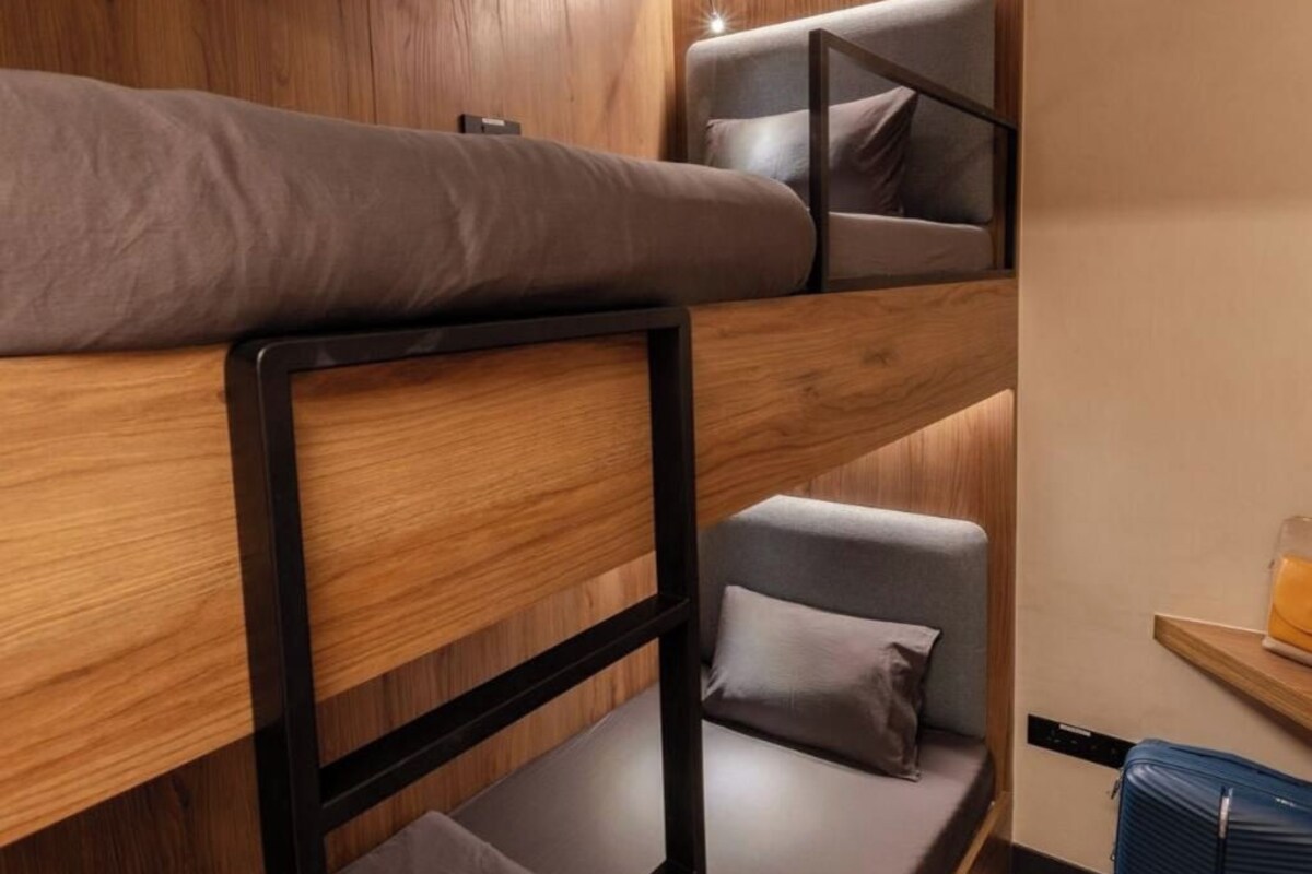 Dormitorio con literas, pared de madera, escritorio y maleta.