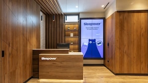 Ett modernt receptionsområde med träpanel och en stor digital skärm som visar reklam för Sleepovers flygplatssovplatser.